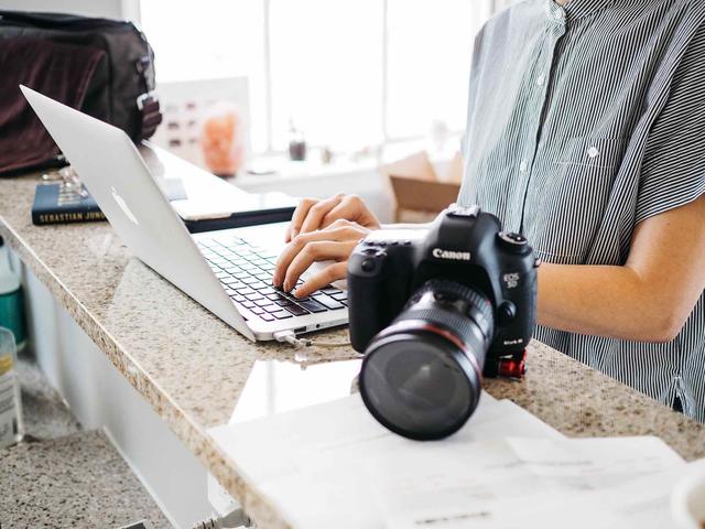 Woman typing on a MacBook next to a camera
