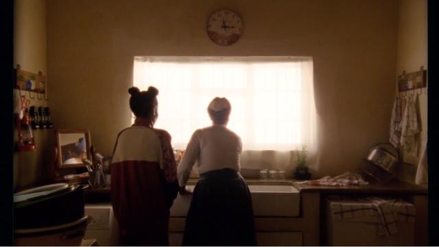 A girl standing in the kitchen behind her mother's back