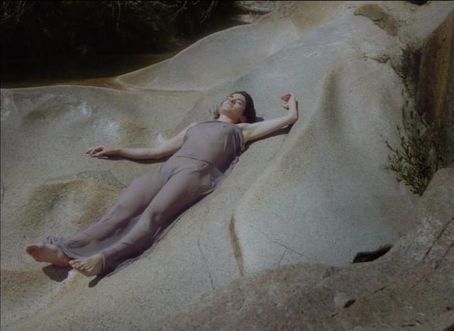 Laura Indigo laying on a beige rock in a thin dress