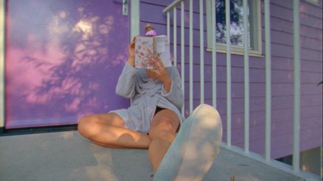 A girl sitting on the pink and white house porch and reading on a sunny summer afternoon